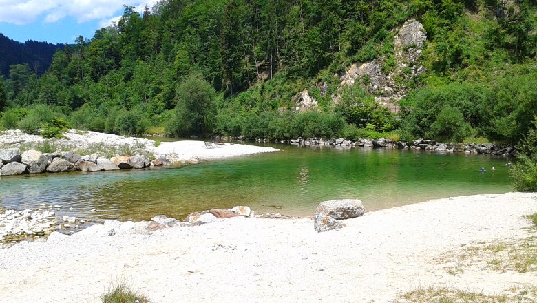 River bath on the Ybbs with green water and a pebble beach, surrounded by wooded hills.