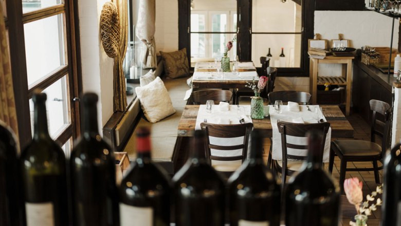 Cozy restaurant with wooden tables and bottles of wine in the foreground.