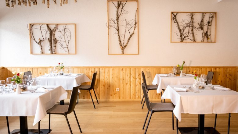 Elegant restaurant with wooden walls, white tablecloths and birch art on the walls.