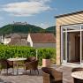 Terrace with tables, chairs and red parasols, Göttweig Abbey on a hill in the background.