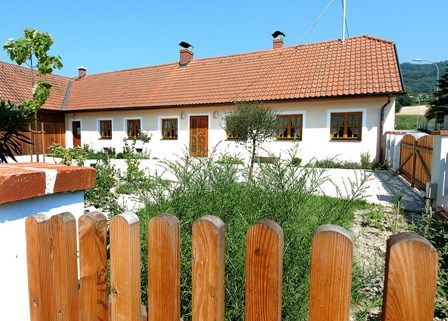 A white vacation home with a red tiled roof and wooden fence in the foreground.