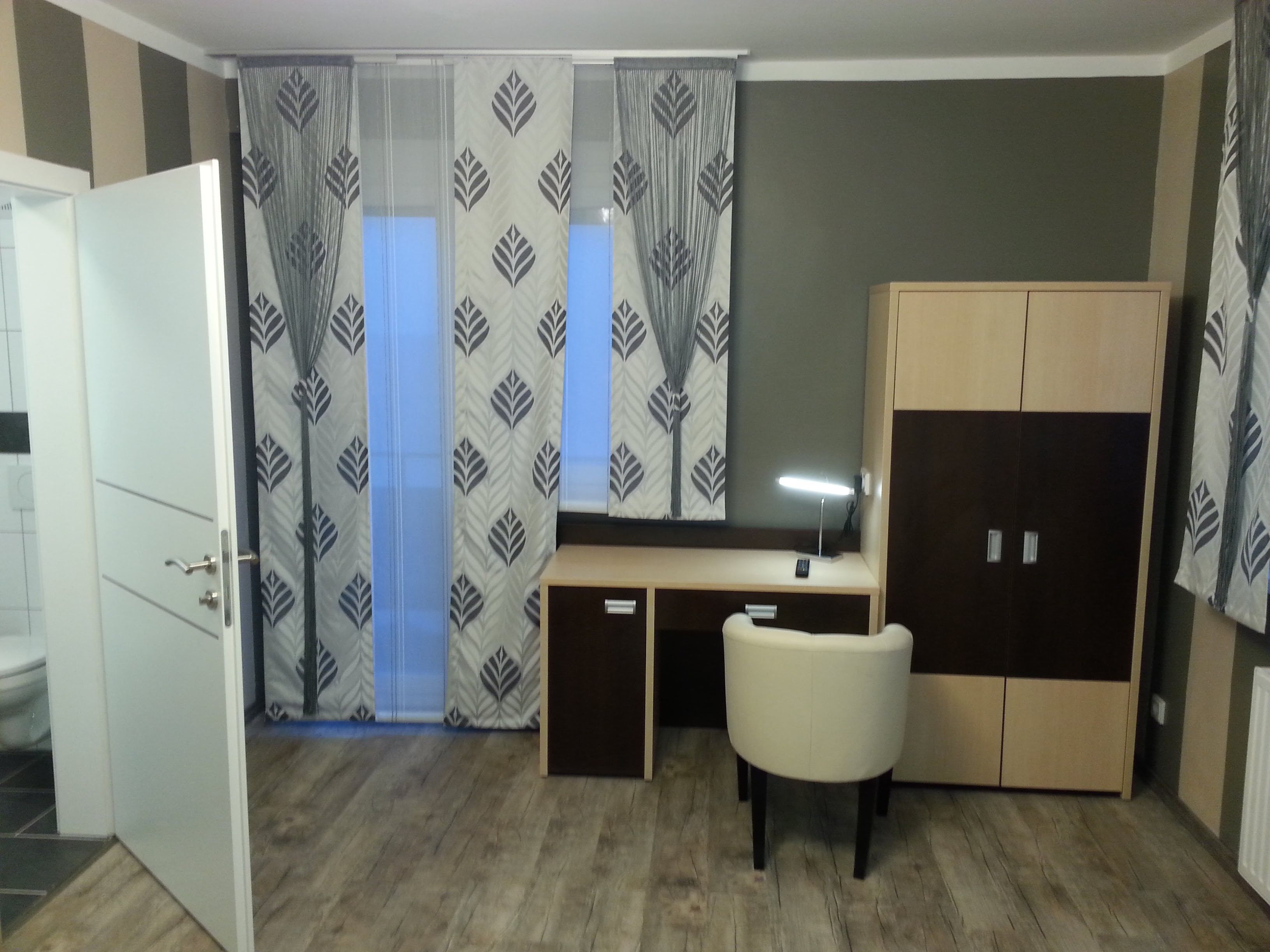 A modern hotel room with desk, chair and closet.