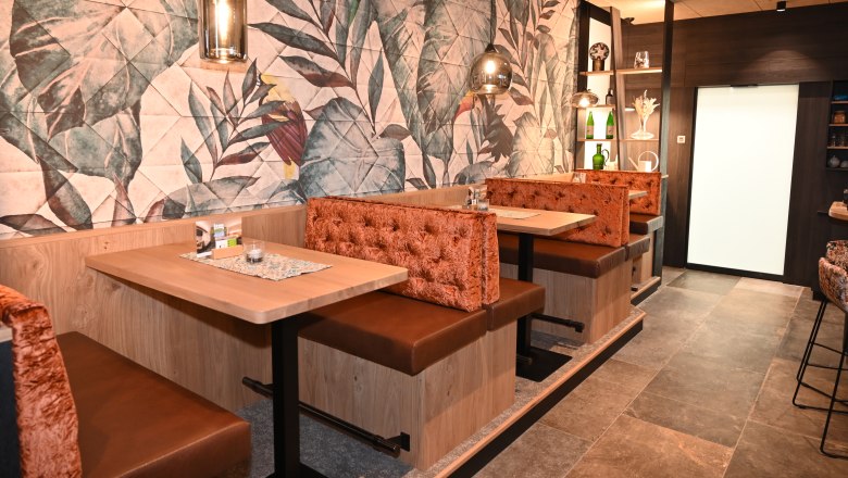 Interior view of a stylish bar with upholstered benches and tropical wall pattern.