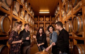 Group of people in a whisky distillery, surrounded by wooden barrels.