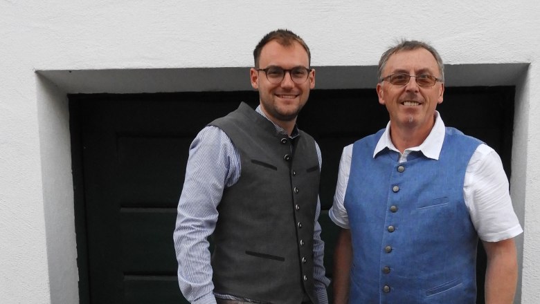 Two men in traditional dress in front of a dark door.