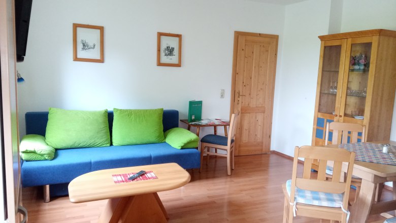 Living room with blue couch, wooden table and chairs, cupboard and pictures on the wall.