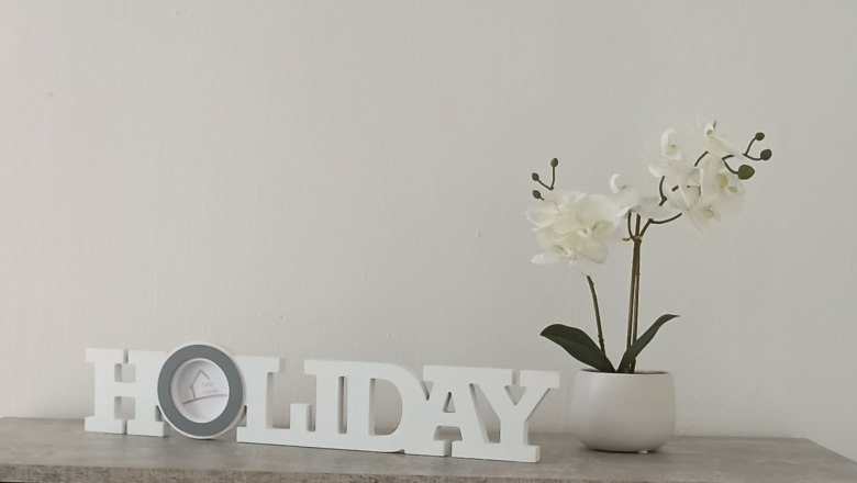Decoration with 'HOLIDAY' lettering and white orchid in a pot on a table.