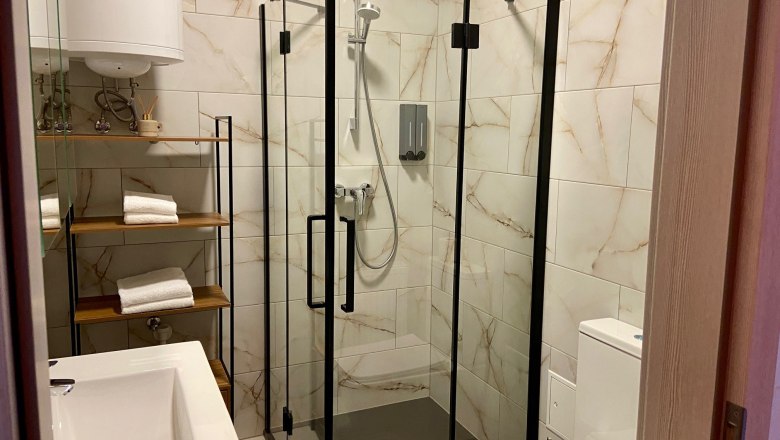 Modern bathroom with glass shower, washbasin, WC and shelf with towels.