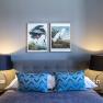 Double room with gray bed, blue pillows, two bedside lamps and bird pictures on the wall.