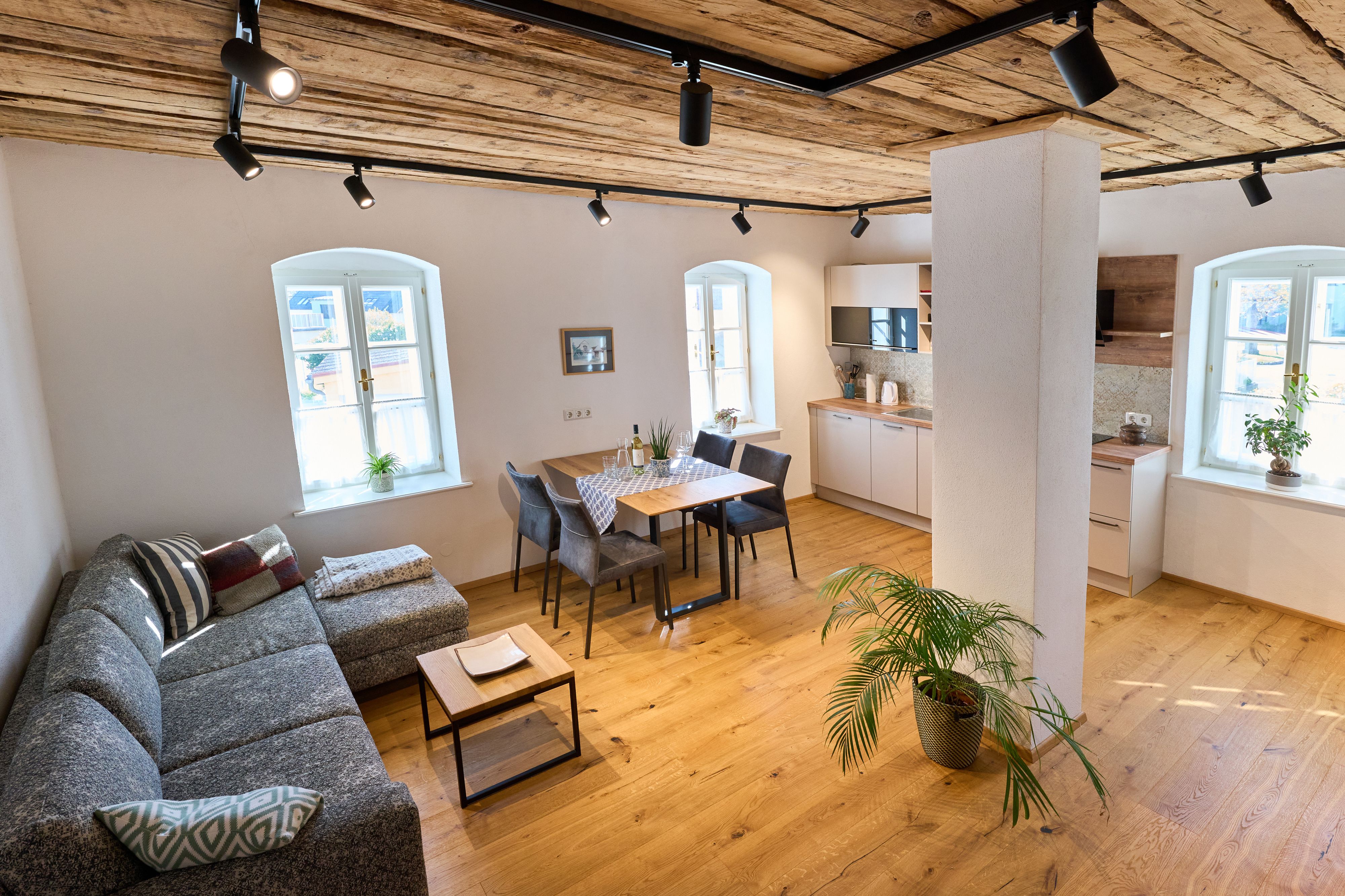 Modern living room with wooden floor, gray sofa, dining table and kitchen.