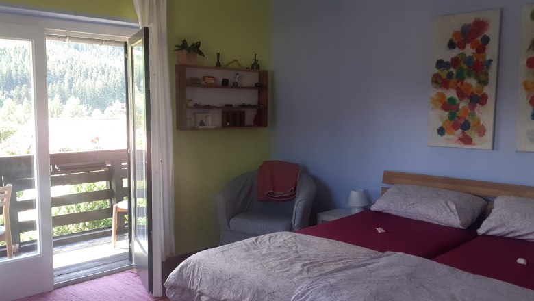 A cozy double room with two beds, a balcony with a view of trees and colorful artwork on the wall.