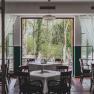 A restaurant with set tables and a view of a green garden through large windows.