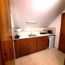 Small kitchenette with wooden cupboards, sink, toaster, kettle and mini-fridge under a sloping roof.