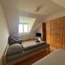 A simply furnished bedroom with two beds, a closet, a TV and an armchair under a sloping roof.