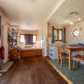 Interior view of a cozy country loft with wooden floor, dining table, chairs, bed and shelves.