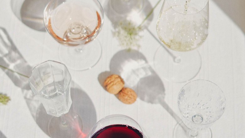 Wine bottle is poured into a glass on a table with various wine glasses and corks.