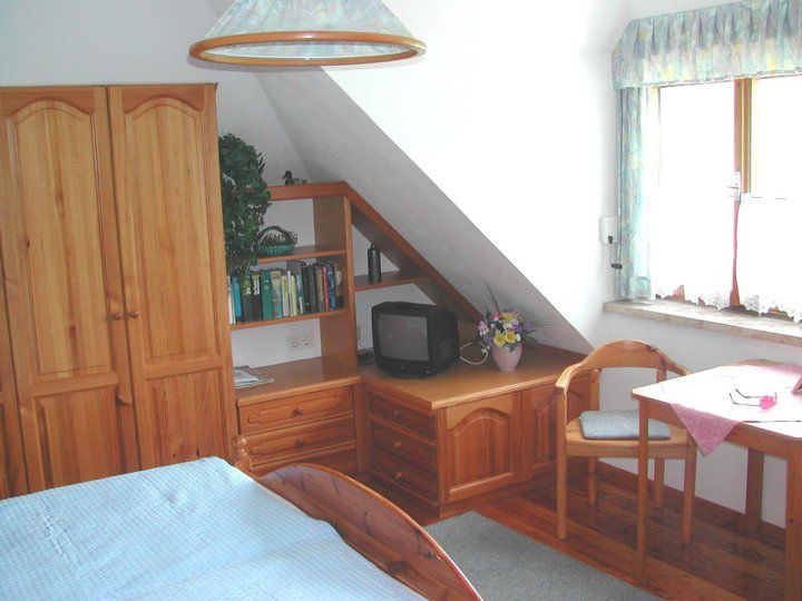 Cozy guest room with wooden furniture, a small TV, a table with chair and a window with curtains.