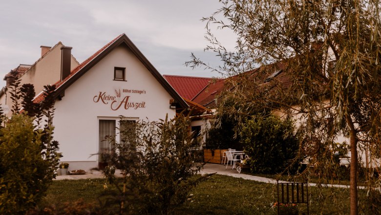 A small building with the inscription 'Biohof Schlager's Kleine Auszeit', surrounded by trees and garden furniture.