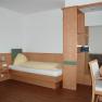 A simply furnished hotel room with a single bed, desk and wooden paneling.