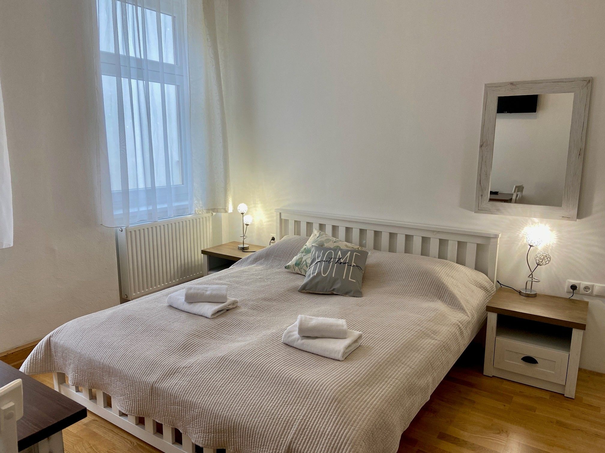 A cozy double room with a large bed, two bedside tables and a mirror on the wall. The room is bright and inviting.