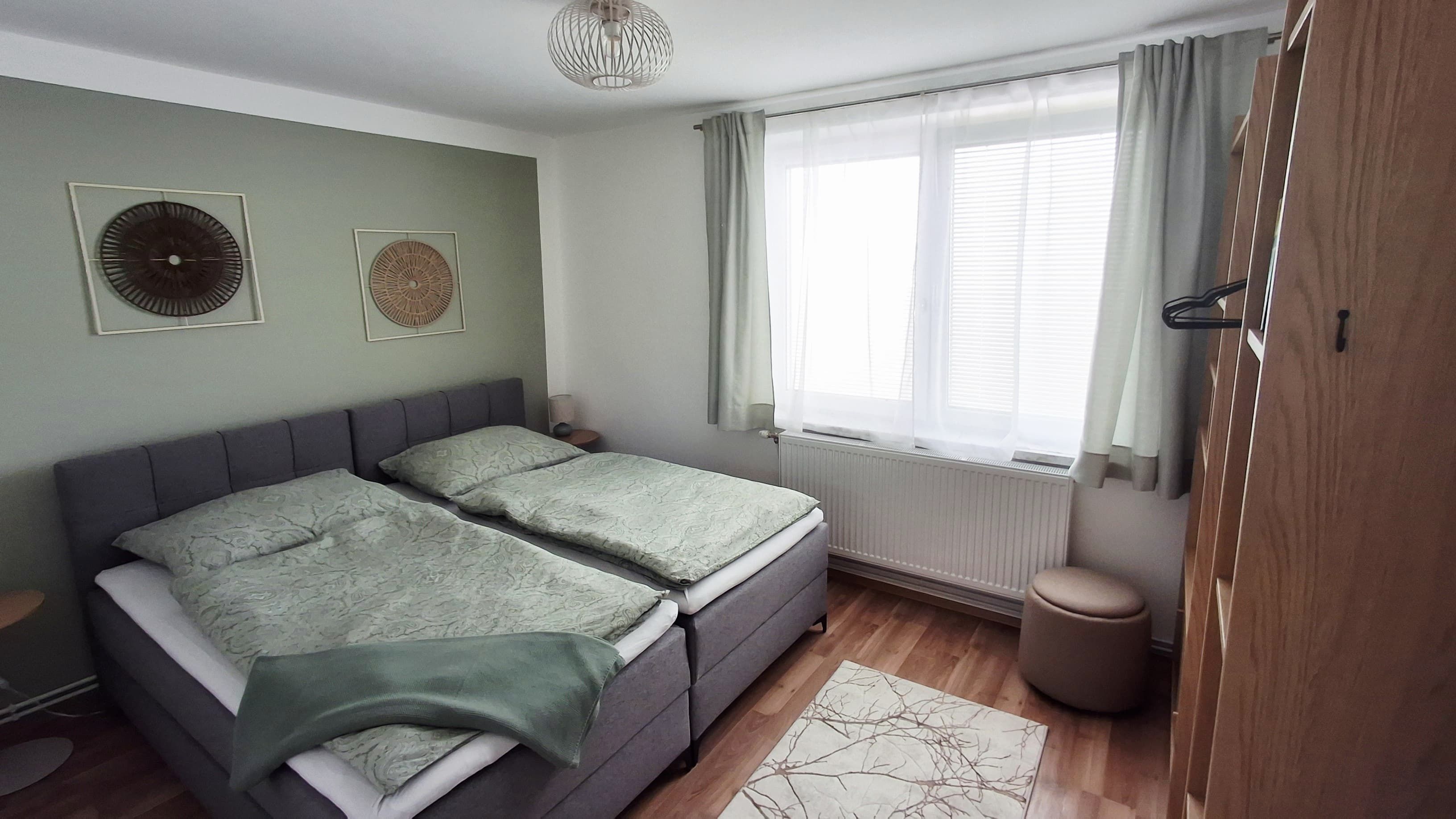 A cozy bedroom with a double bed, green bed linen, wooden furniture and decorative murals.