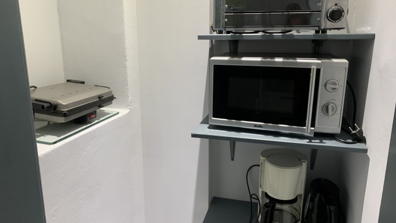 Kitchen shelf with toaster, microwave, coffee machine and kettle.