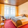 Comfortable hotel room with double bed, wooden furniture and red carpet.