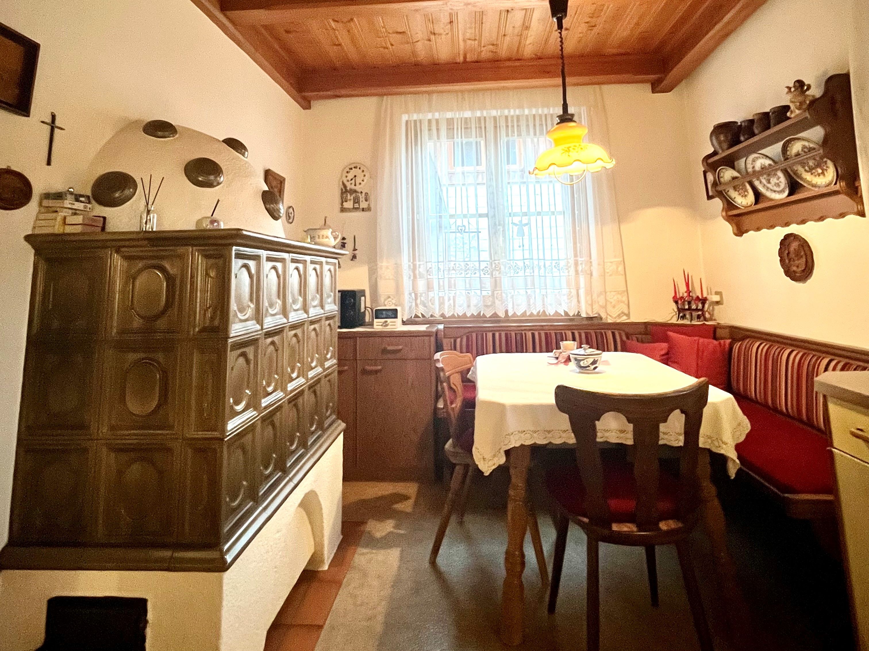 Cozy kitchen with tiled stove, wooden table and corner bench.