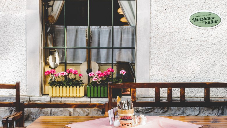 A table with cutlery holders and spices in front of a window with flowers and musical instruments.