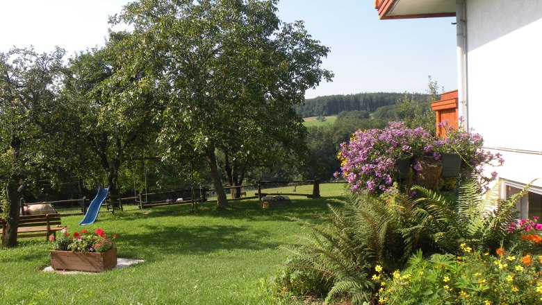 A green garden with trees, flowers and a blue slide.