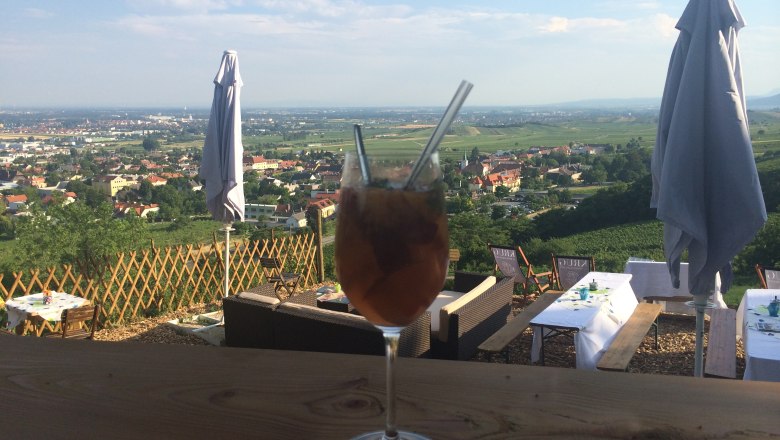A drink in a wine glass with straws in front of a landscape of tables and parasols.