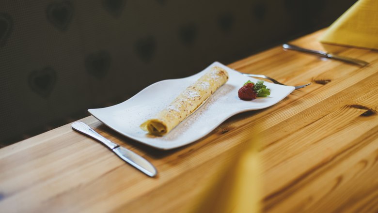 A pancake on a white plate with strawberry and mint, served on a wooden table.
