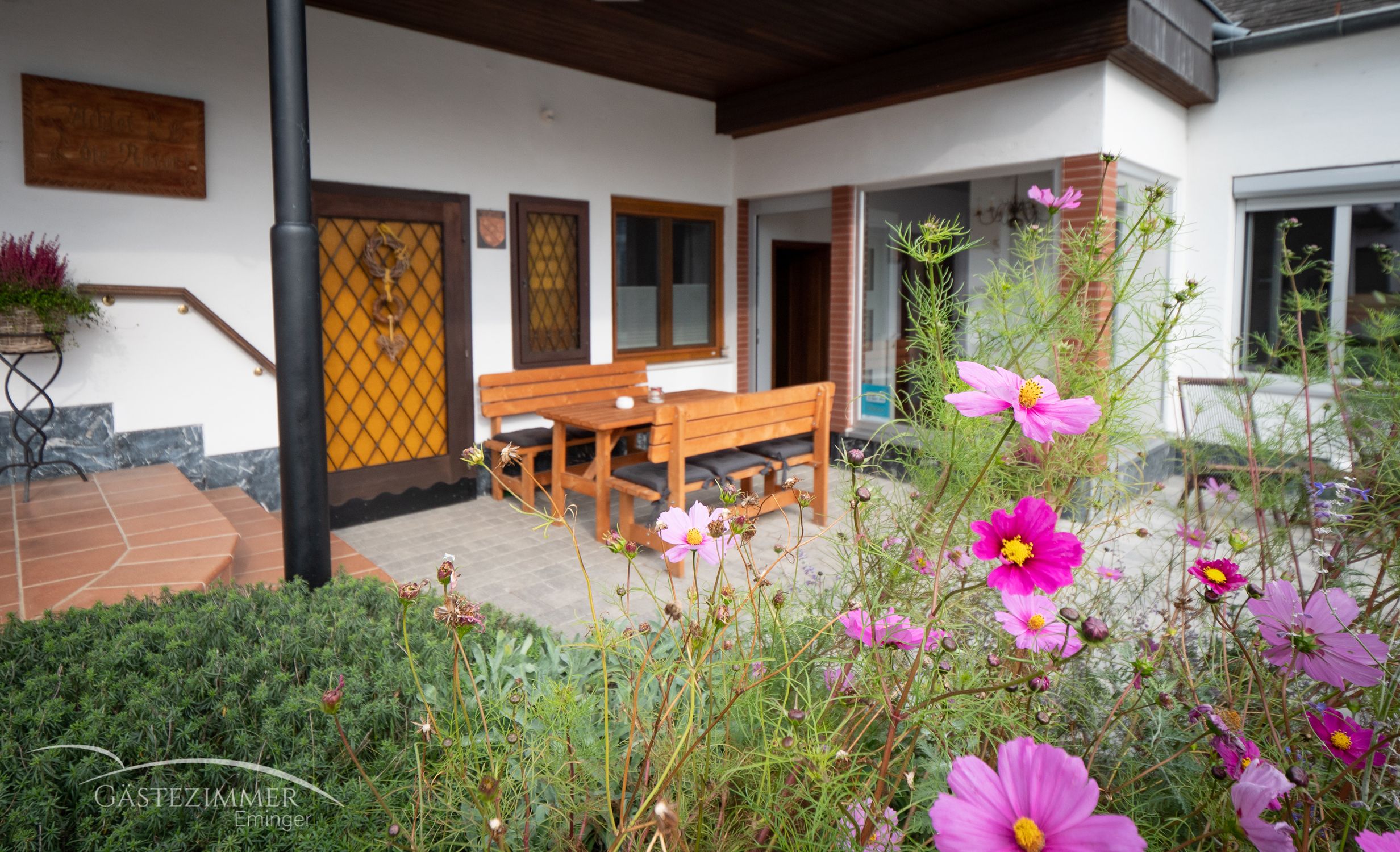 Terrace with wooden furniture and blooming flowers in the foreground.