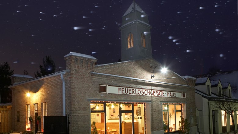 Old fire station at night with lights and snowfall.