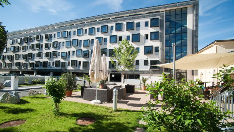 Modern building with many windows and garden area with seating.