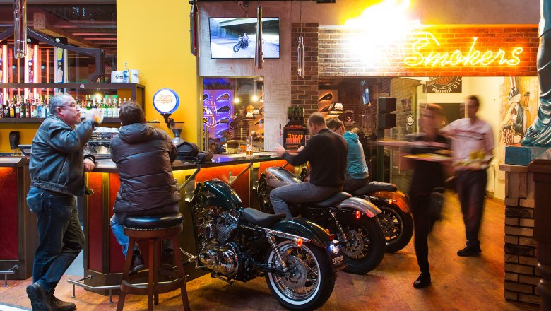Bar with motorcycles as seating, neon light and guests.
