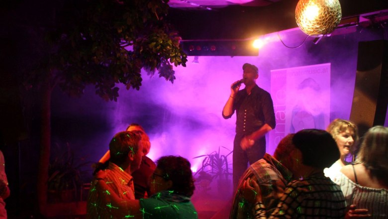 A singer on a stage with a microphone, surrounded by dancing couples and colorful lights.