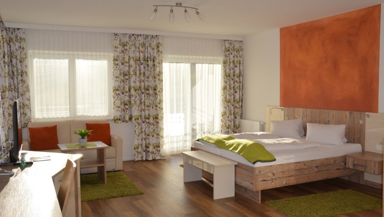 A modern double room with wooden floor, a double bed, sofa, table and large windows with curtains.