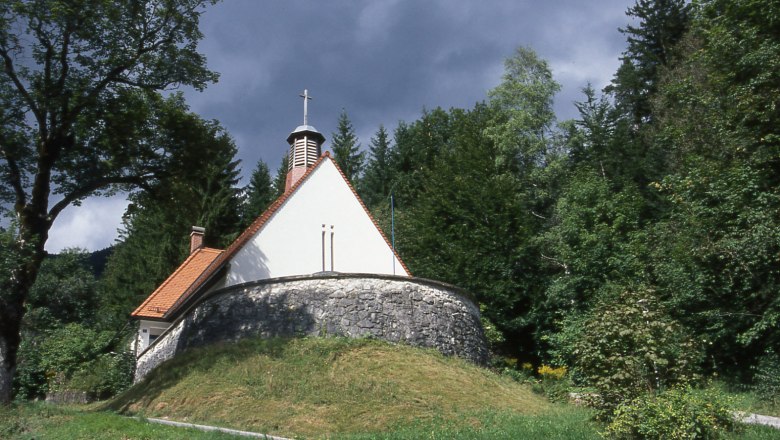 Small church in the forest with a stone base and red roof.
