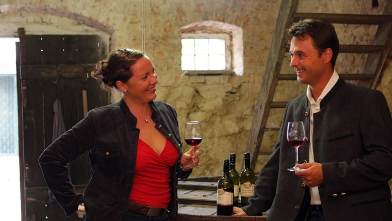 Two people at a wine tasting in a rustic room.