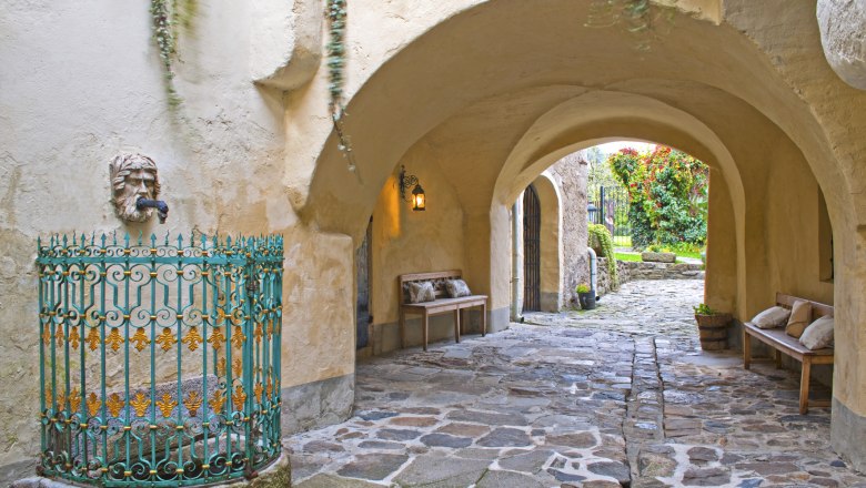 Passage, © Renaissancehotel “ Raffelsberger Hof “ A stone passageway with benches, a lantern and an ornate fountain.