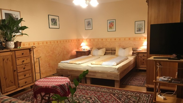 Cozy bedroom with wooden furniture, double bed, carpet and plants.
