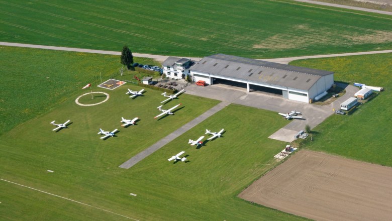 Aerial view of a small airfield with several parked airplanes and a hangar.