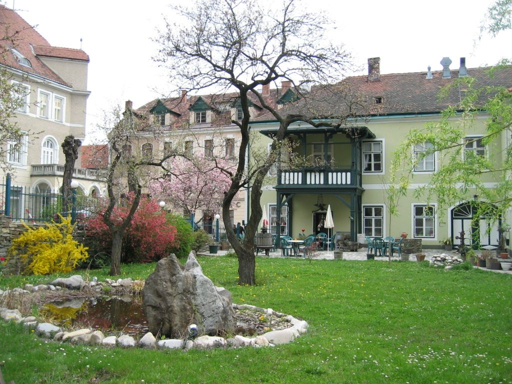 A garden with a pond and trees in front of a historic building with a balcony.