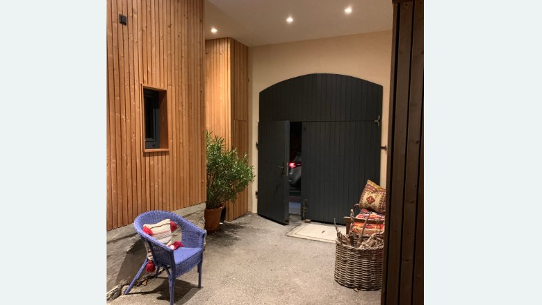 An inner courtyard with wooden walls, a blue chair, a plant and a large black gate.