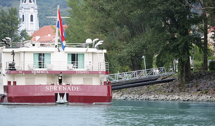 A river cruise ship named Serenade at a landing stage in D&uuml;rnstein, with a church tower in the background.