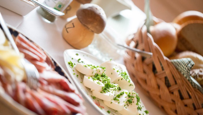 A breakfast table with cheese, ham, bread rolls and herbs.