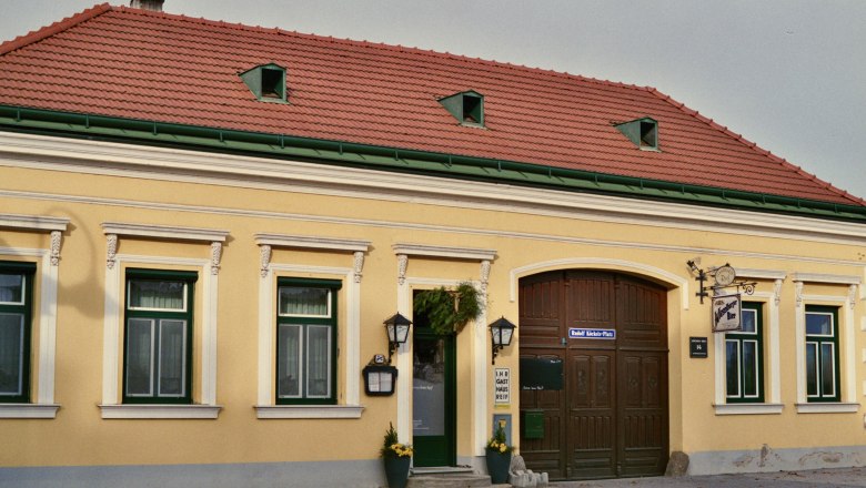 Exterior view of a yellow inn with red roof tiles and green window frames.