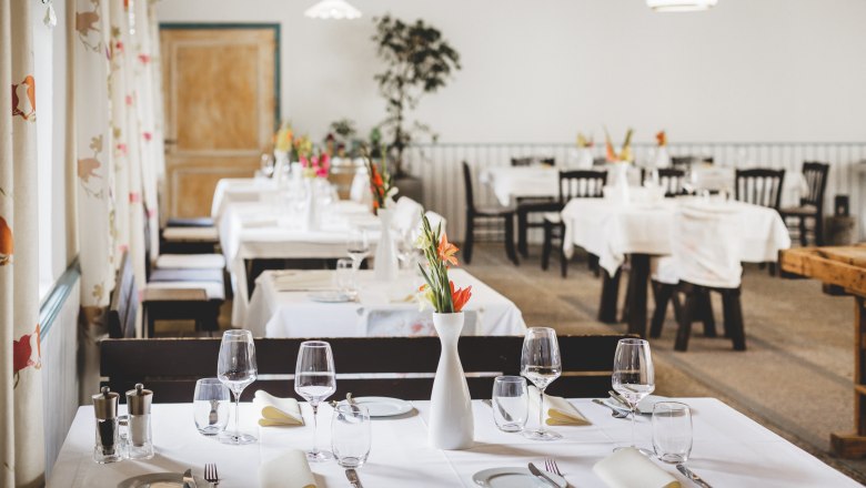 Elegant restaurant with white-clothed tables and flower vases.