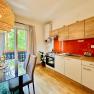 Modern kitchen with wooden units, red splashback and dining table in front of a window with a view of the greenery.